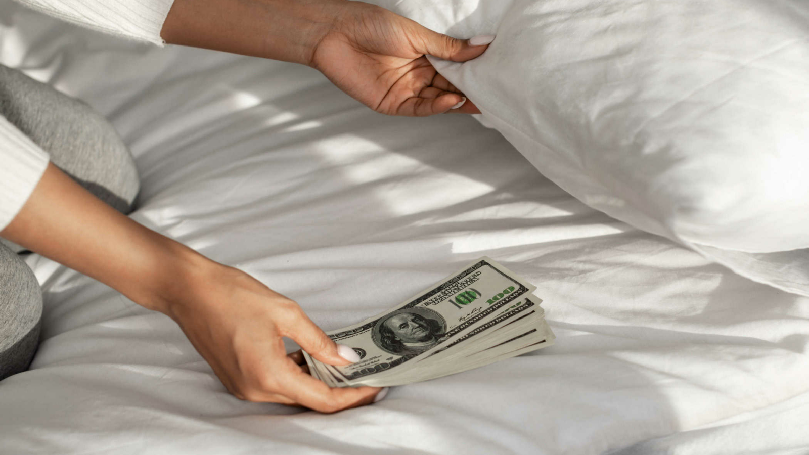 Closeup of unrecognizable millennial African American woman hiding money under pillow at home. Wealth, Financial Safety And Literacy, Distrust In Banking Services Concept.