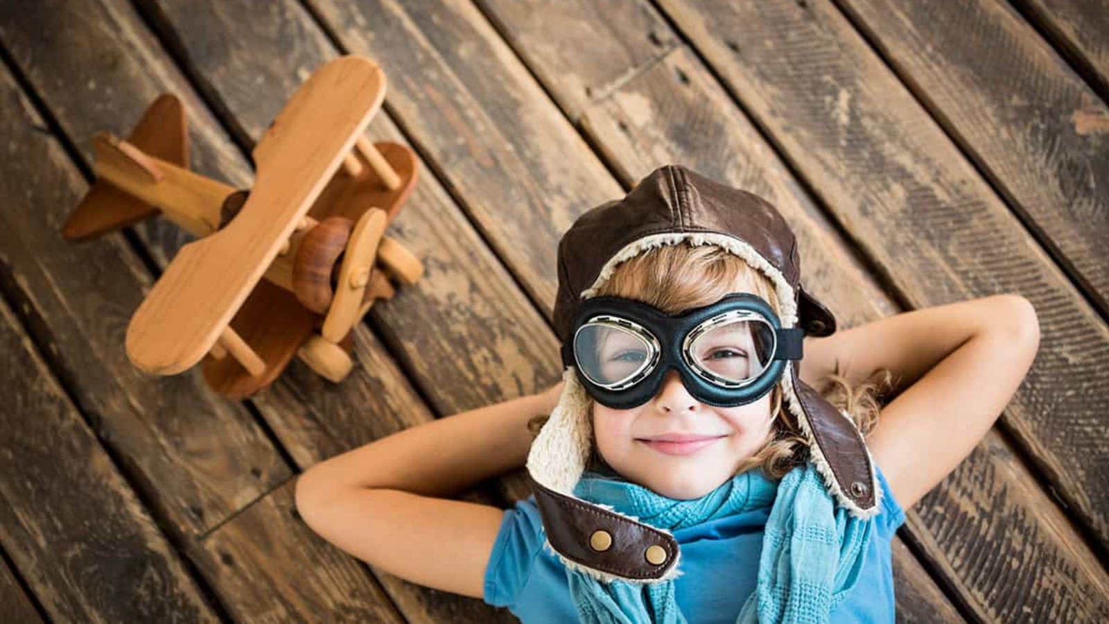 Child pilot with vintage plane toy on grunge wooden background