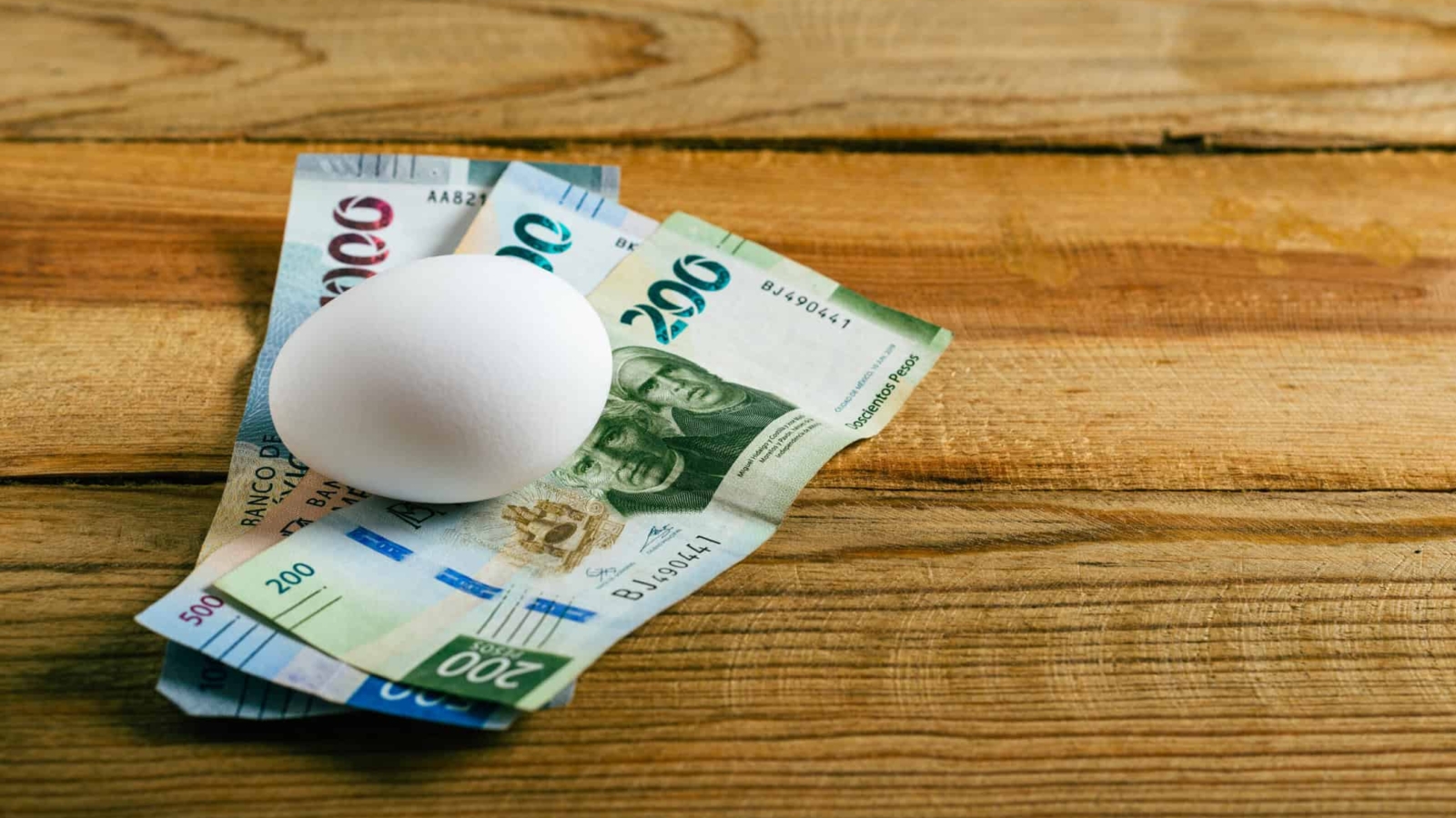 Egg and Mexican banknotes on wooden table. Concept of rising cost of egg production and consumption.