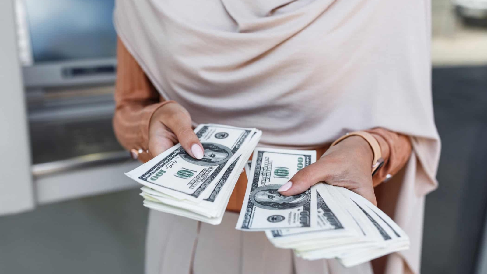 Finance, money transfer, banking, ATM, modern technology, win, withdraw, currency and social distancing. Young unrecognizable arab female in hijab holding a lot of dollars, counting cash, close up