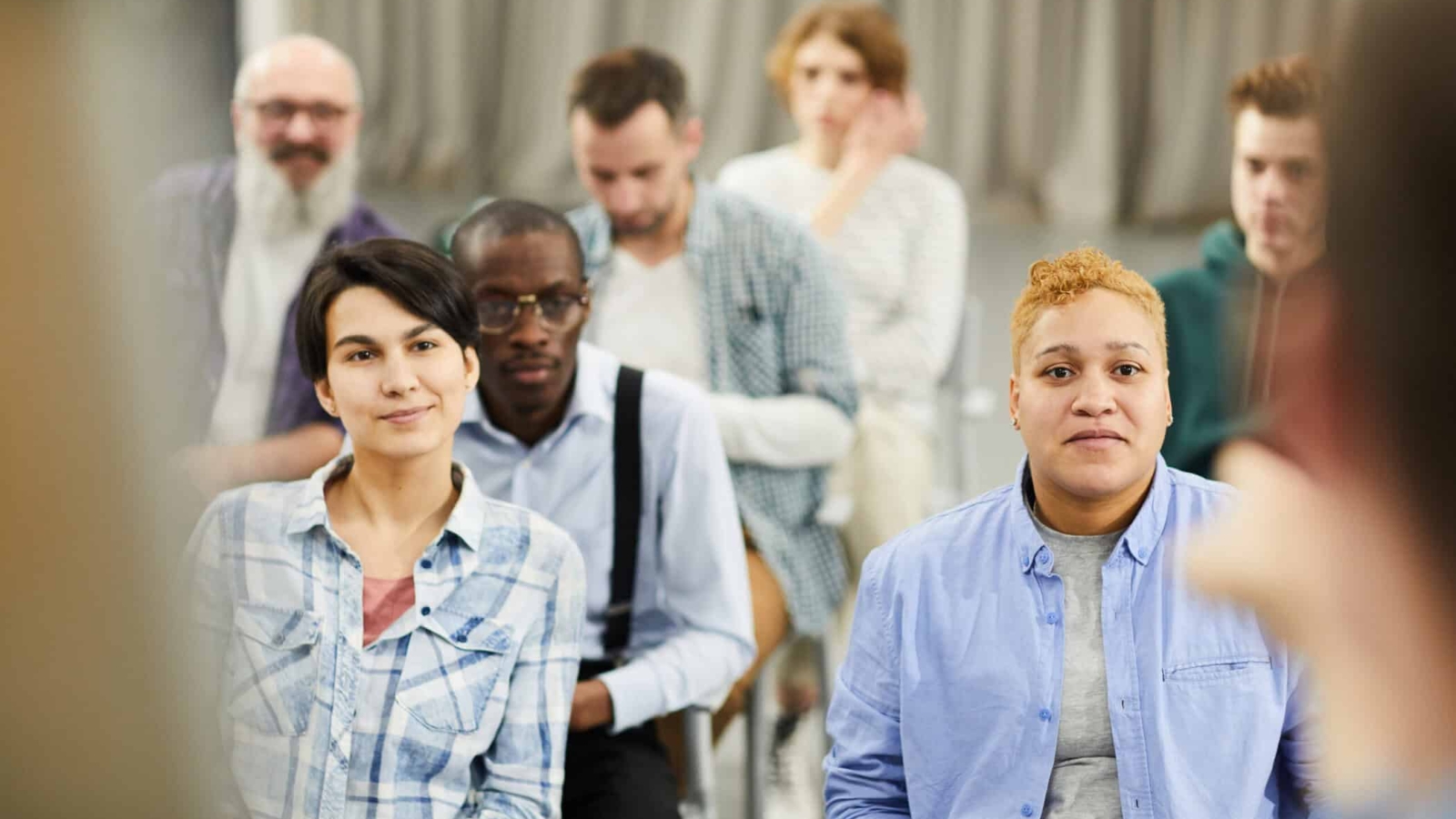 Group of content curious people in casual clothing sitting on chairs and listening to speaker during conference