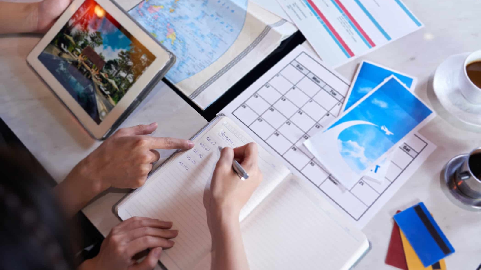 Close-up shot of unrecognizable couple taking necessary notes and planning vacation trip to Europe while sitting at table